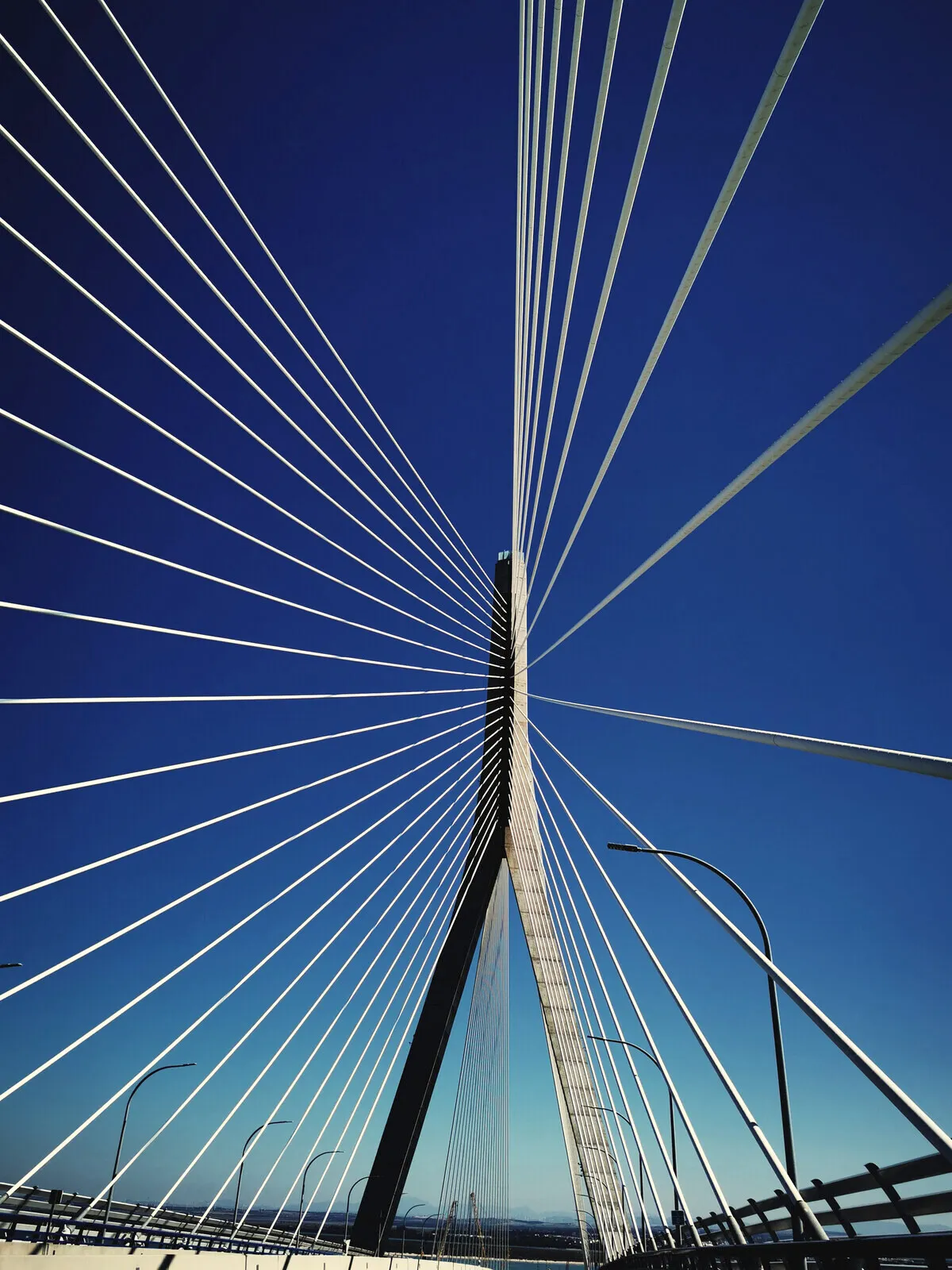 The cables of a bridge in Cádiz, fanning out into a deep blue sky.