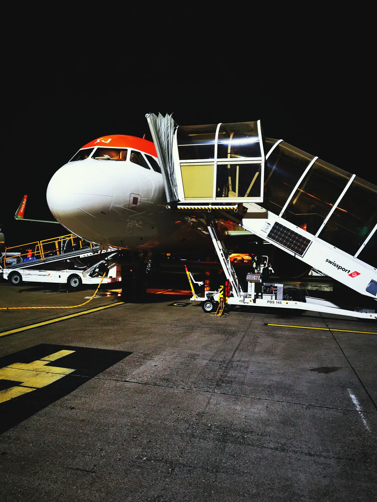An easyJet aircraft at its gate before dawn, air bridge attached.