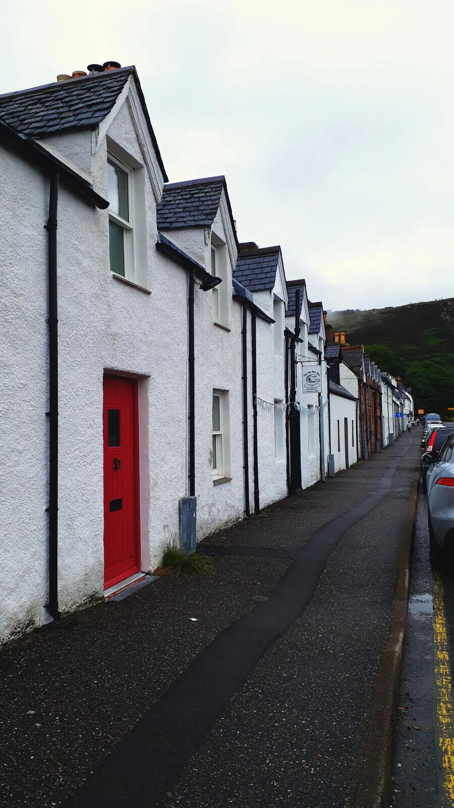 A row of white cottages in Ullapool, one door painted red.