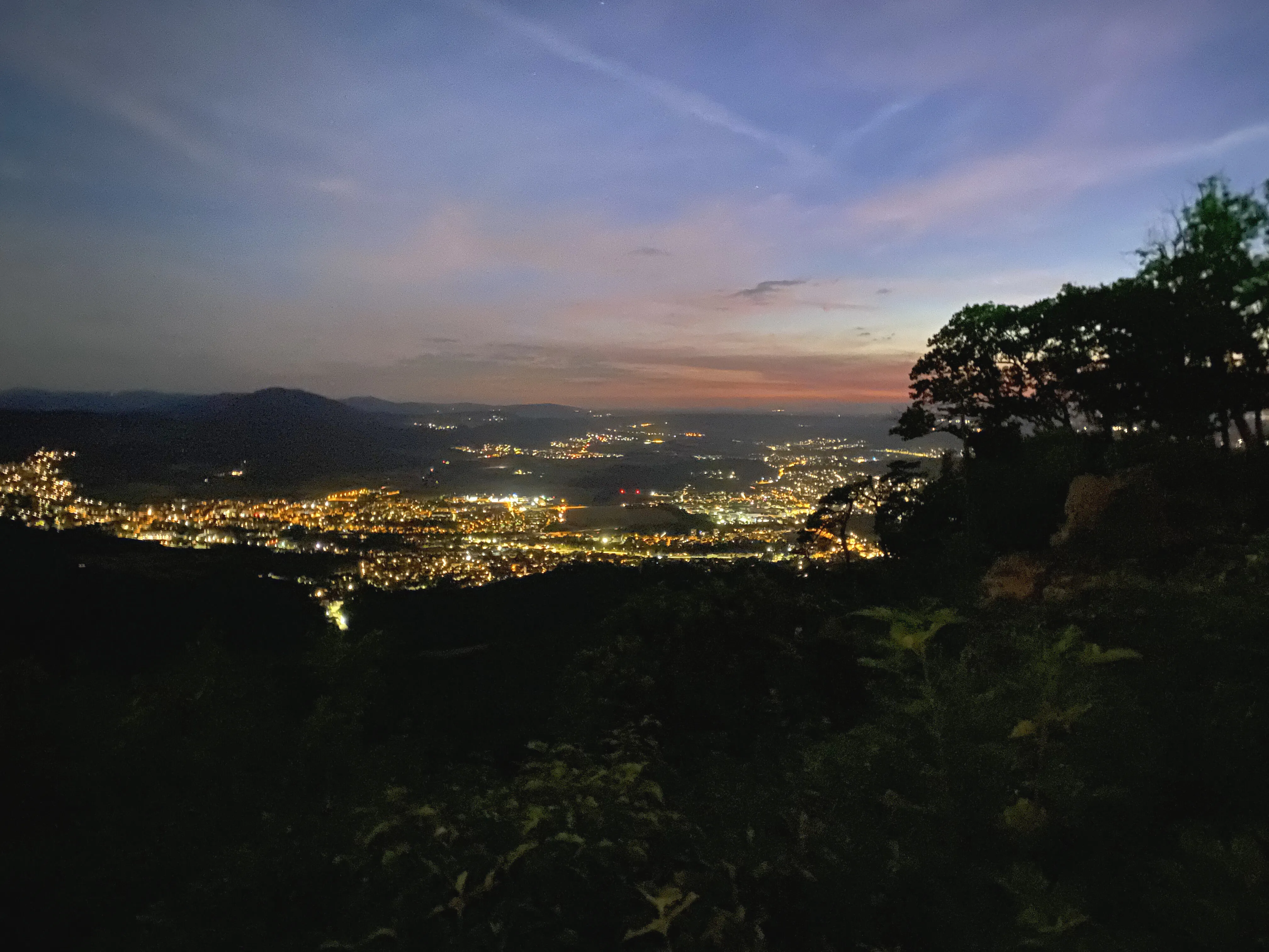 The lights of a valley town at dusk, from the slope above.