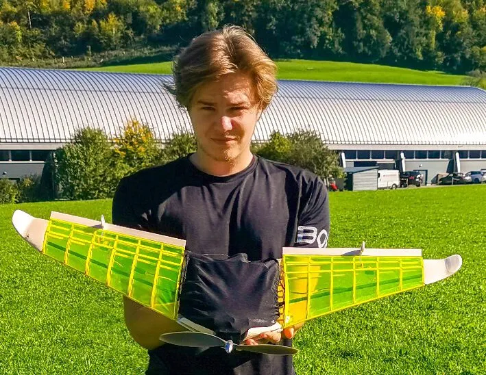 Holding a model flying wing on a field.